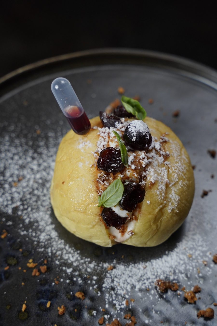 Brioche farcita con crema, ciliegie scure, basilico e zucchero a velo, con una pipetta di sciroppo