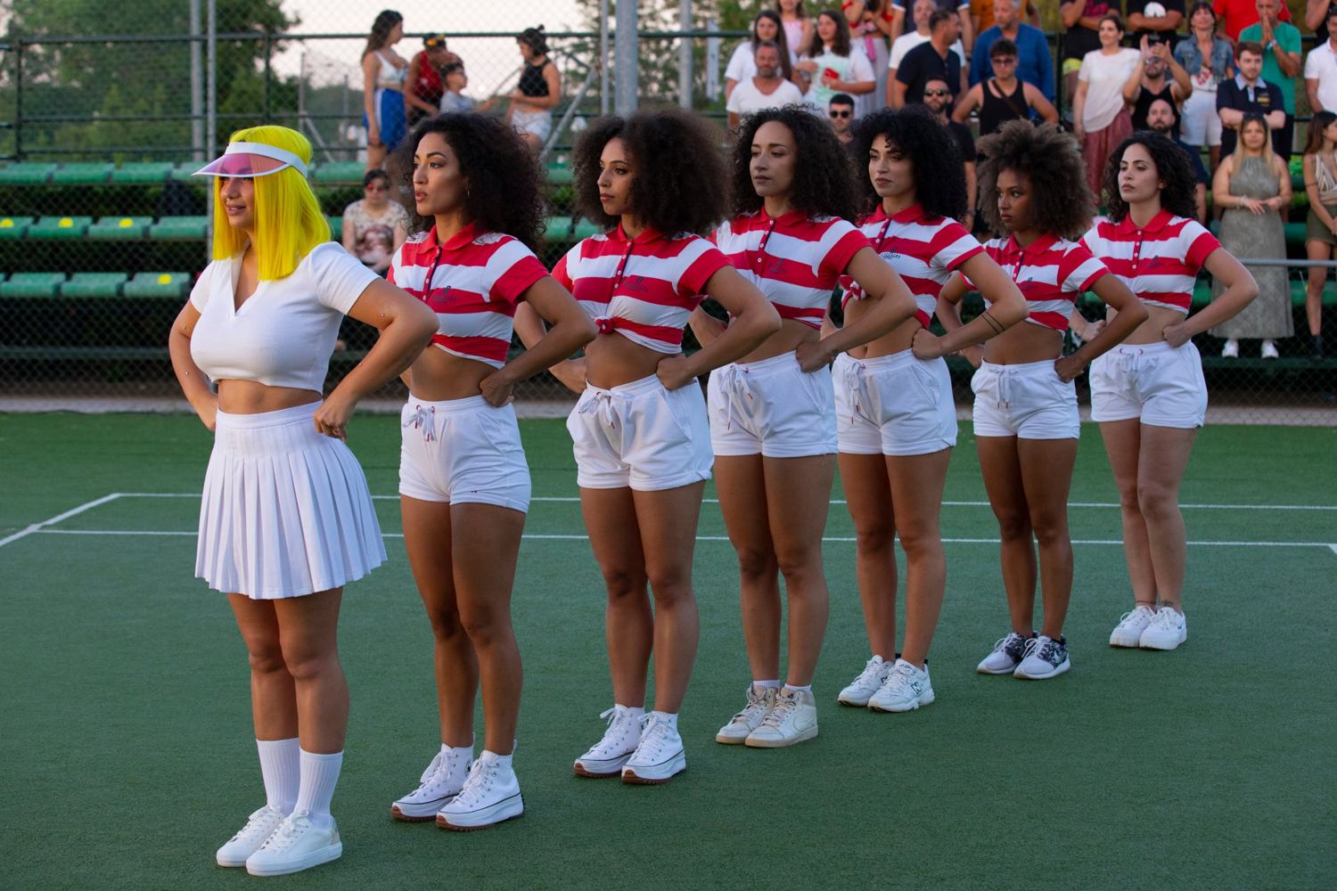 La donna con il caschetto giallo e sei ballerine in fila sul campo da tennis, con le mani sui fianchi