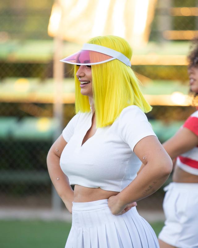 Una donna con caschetto giallo fluo e visiera rosa che ride su un campo da tennis