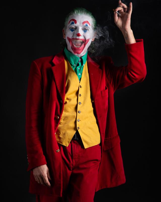 Un attore truccato da Joker che ride su fondo nero, con il fumo di una sigaretta